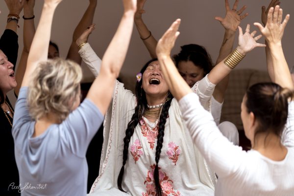 A joyful woman with braids celebrates amidst a group, expressing emotion in a serene indoor yoga gathering.