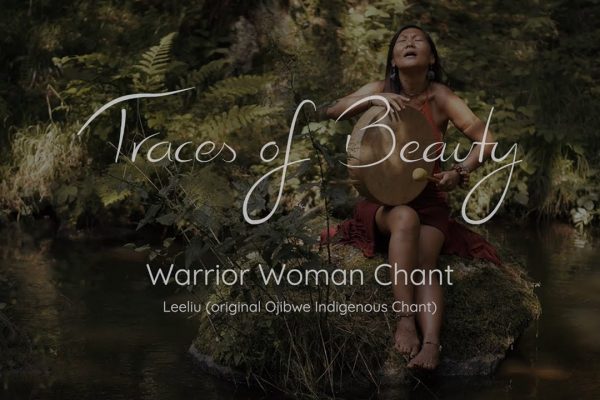 A woman in natural surroundings performs the Warrior Woman Chant while playing a drum, evoking a serene atmosphere.