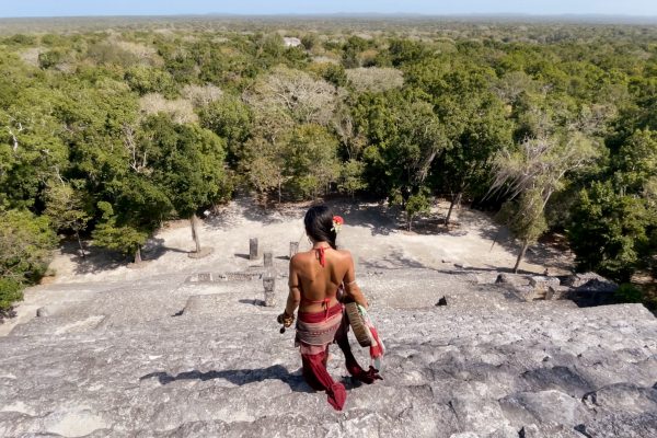 Person in traditional attire descends stone steps overlooking a lush, green landscape, likely a cultural or historical site.
