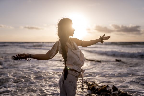 Silhouette of a woman with outstretched arms against the sunset at a beach, reflecting a serene and joyful atmosphere.